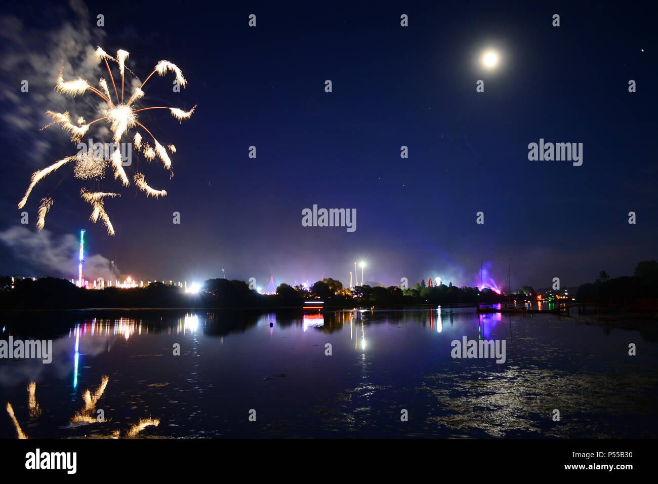 Newport, Isle of Wight, UK. 24th June, 2018. Fireworks and a near full moon herald the end of the last day of the Isle of Wight Festival as the Sunday night headliner band 'The Killers' play on the main stage, seen in the distance in bright lights. Photograph taken from the banks of the River Medina in Newport, Isle of Wight, June 24th 2018. Credit: Matthew Blythe/Alamy Live News Stock Photo