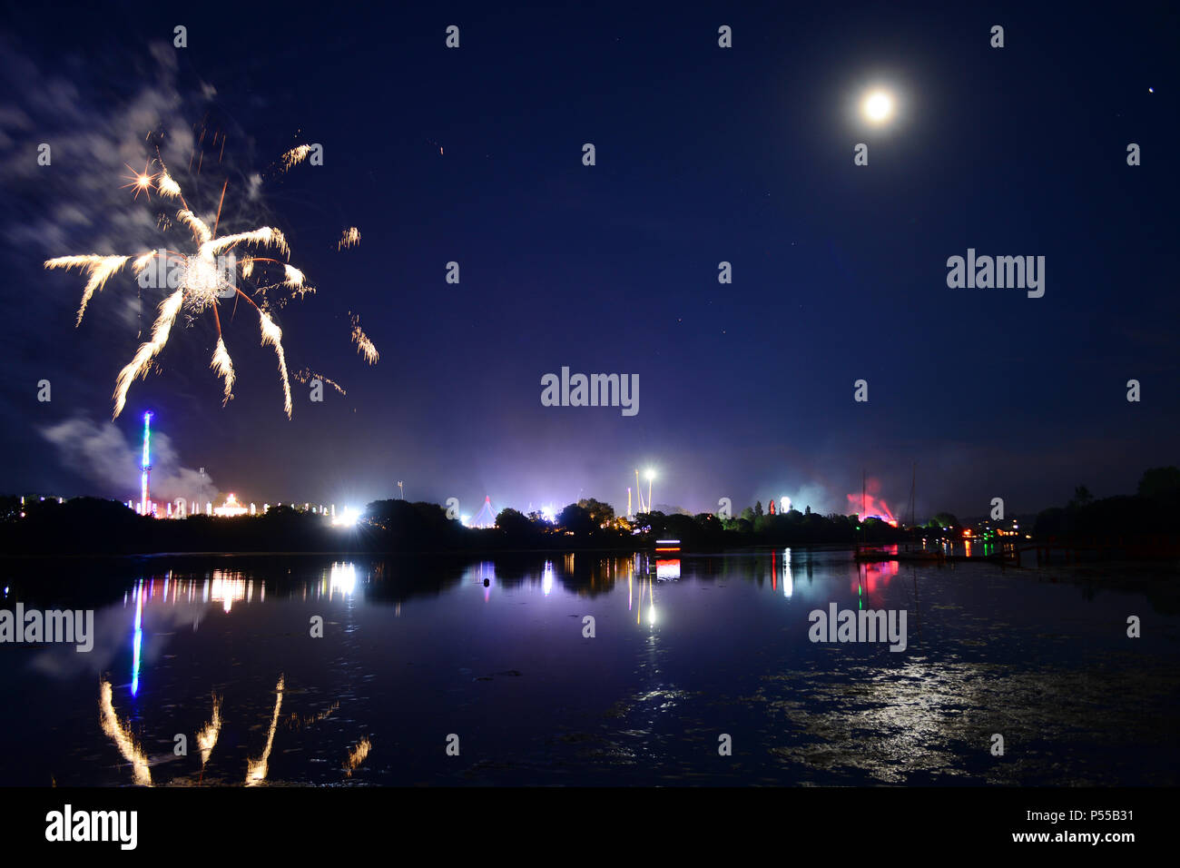 Newport, Isle of Wight, UK. 24th June, 2018. Fireworks and a near full moon herald the end of the last day of the Isle of Wight Festival as the Sunday night headliner band 'The Killers' play on the main stage, seen in the distance in bright lights. Photograph taken from the banks of the River Medina in Newport, Isle of Wight, June 24th 2018. Credit: Matthew Blythe/Alamy Live News Stock Photo