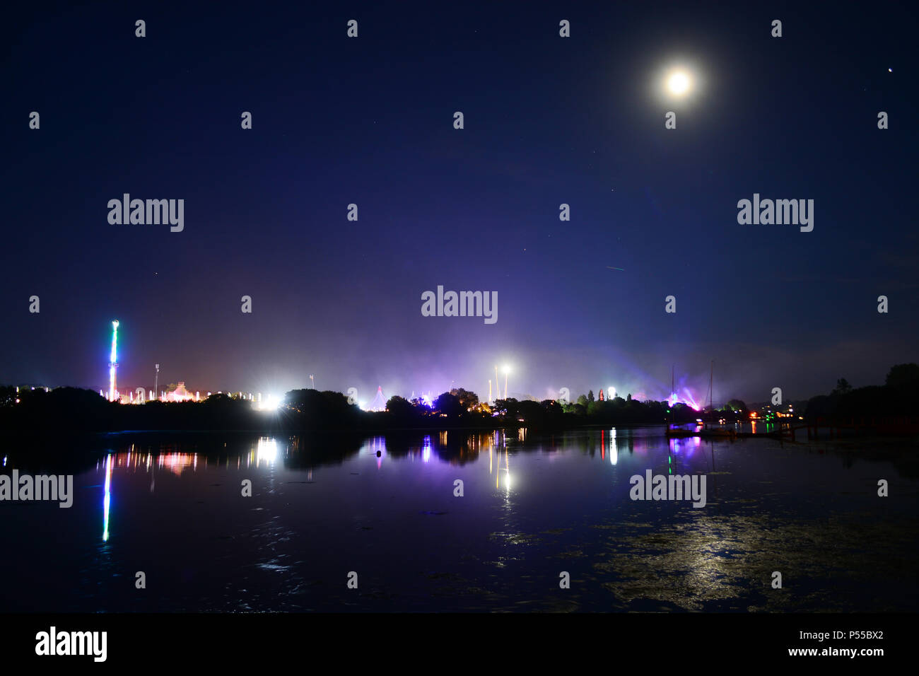 Newport, Isle of Wight, UK. 24th June, 2018. Fireworks and a near full moon herald the end of the last day of the Isle of Wight Festival as the Sunday night headliner band 'The Killers' play on the main stage, seen in the distance in blue lights. Photograph taken from the banks of the River Medina in Newport, Isle of Wight, June 24th 2018. Credit: Matthew Blythe/Alamy Live News Stock Photo