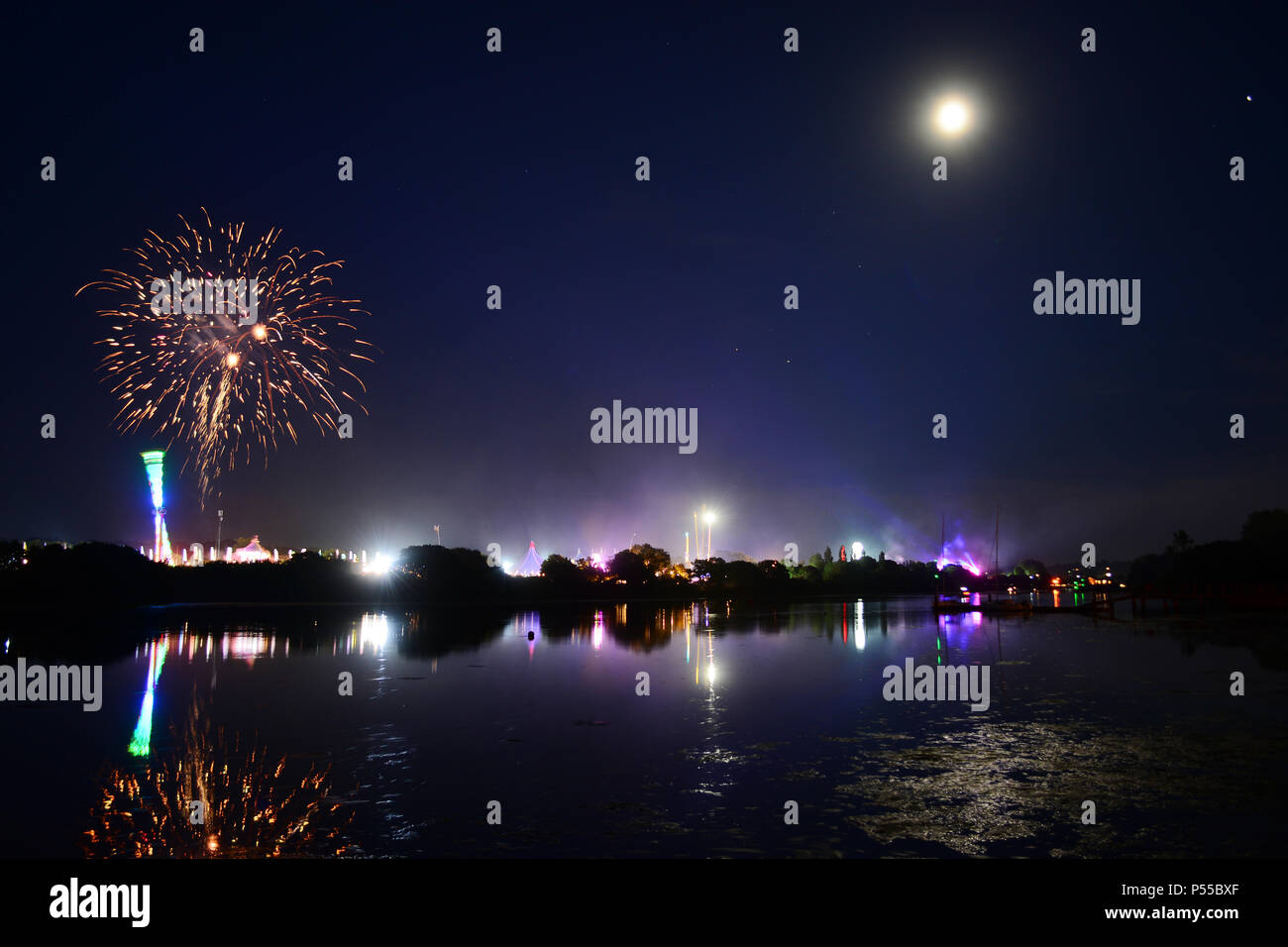 Newport, Isle of Wight, UK. 24th June, 2018. Fireworks and a near full moon herald the end of the last day of the Isle of Wight Festival as the Sunday night headliner band 'The Killers' play on the main stage, seen in the distance in blue lights. Photograph taken from the banks of the River Medina in Newport, Isle of Wight, June 24th 2018. Credit: Matthew Blythe/Alamy Live News Stock Photo