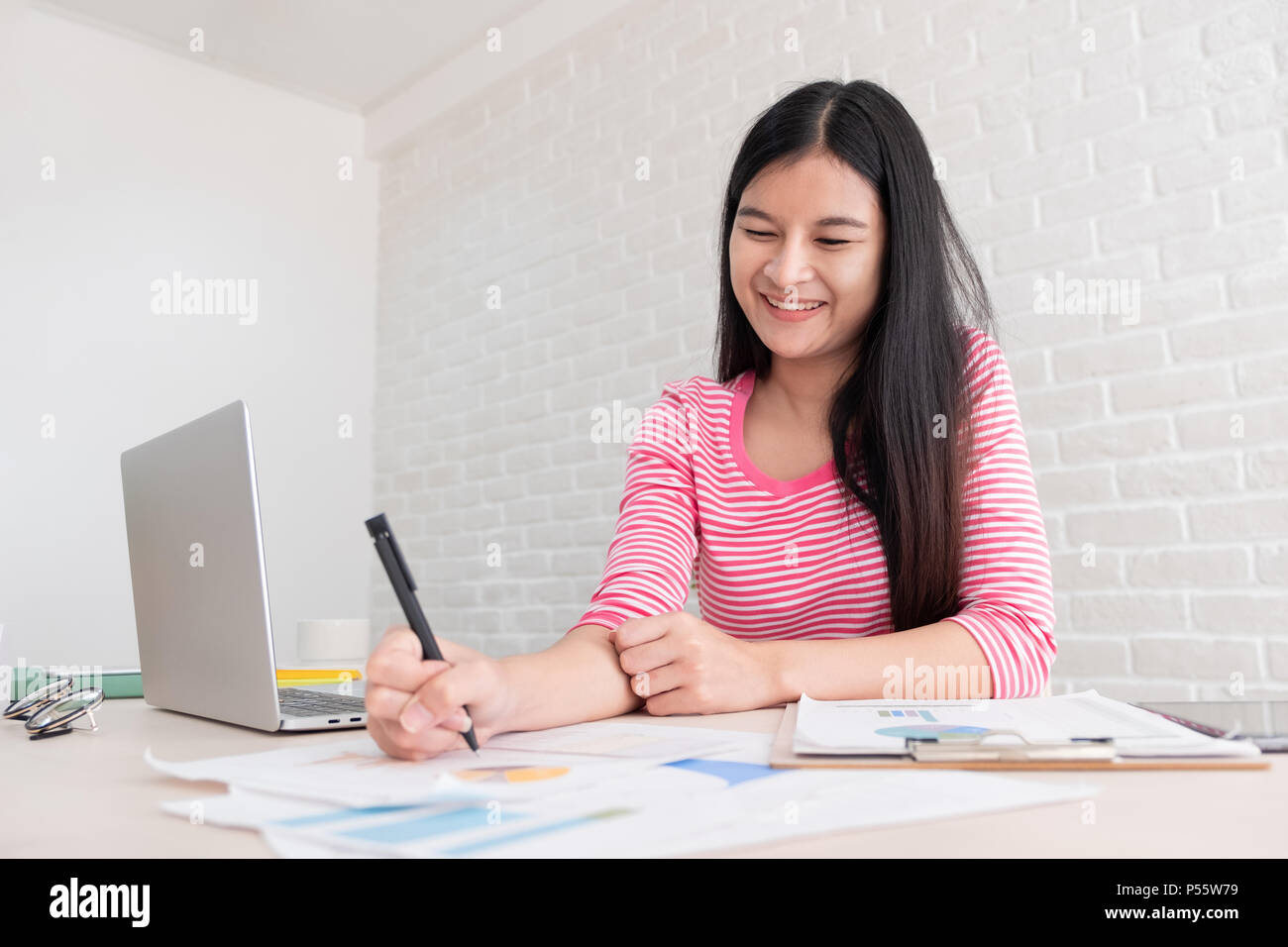 Asian female freelancer working on laptop computer on table at brick wall at home.working online lifestyle Stock Photo