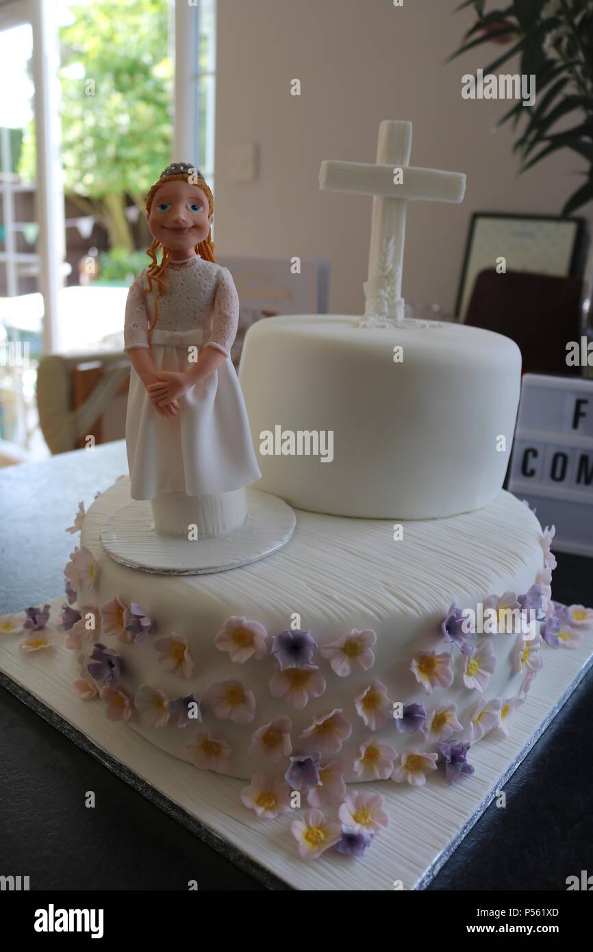 Two tier Catholic first communion cake with icing figure of a girl, white cross and lilac and lemon flowers and light box saying first communiom Stock Photo