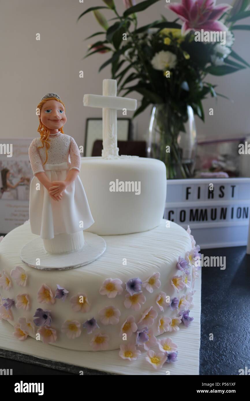 Two tier Catholic first communion cake with icing figure of a girl, white cross and lilac and lemon flowers and light box saying first communiom Stock Photo