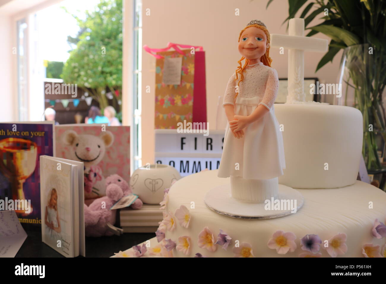 Two tier Catholic first communion cake with icing figure of a girl, white cross and lilac and lemon flowers and light box saying first communiom Stock Photo