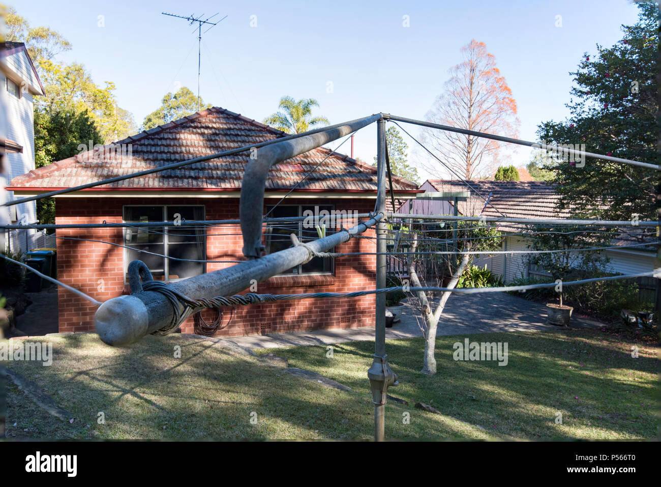 A  well preserved early1960s Hills Hoist clothes drying line in a backyard and a red brick tile roof home from 1964 in Australia Stock Photo