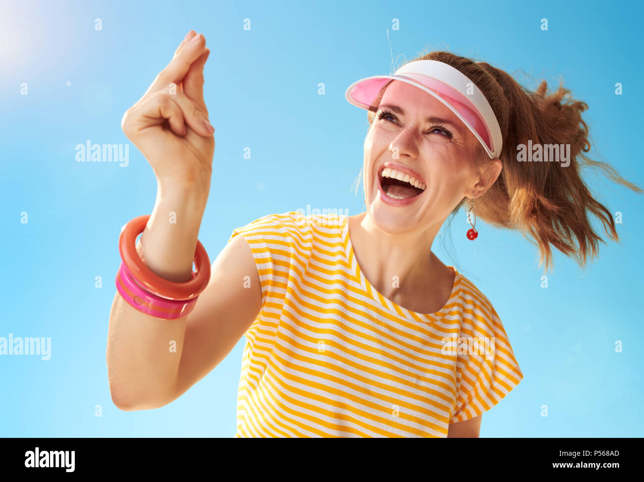smiling young woman in yellow shirt against blue sky fingers snapping Stock Photo