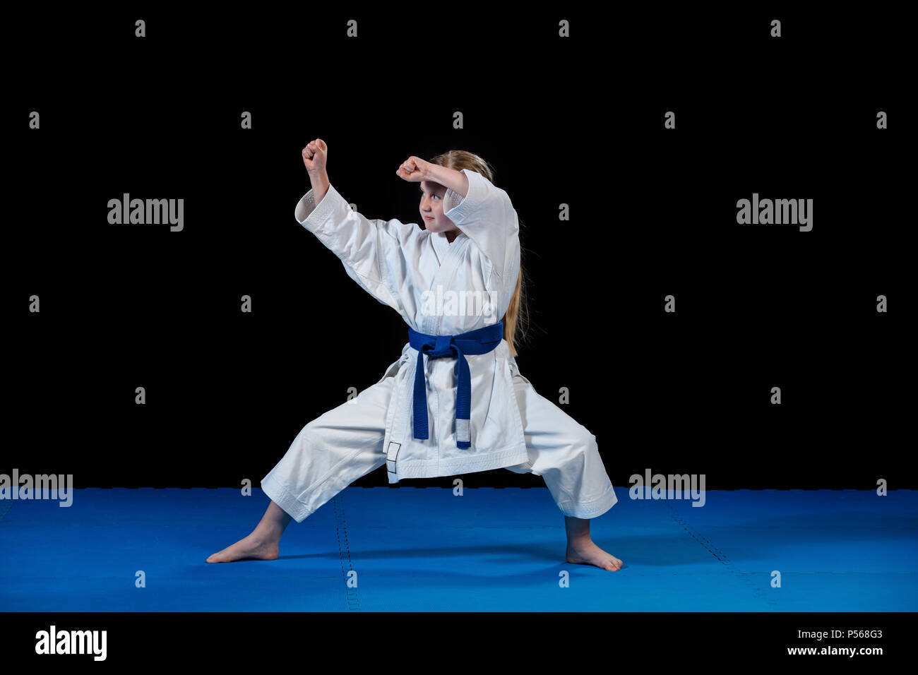 sweet little girl in martial arts practice like karate kid alone isolated on black background