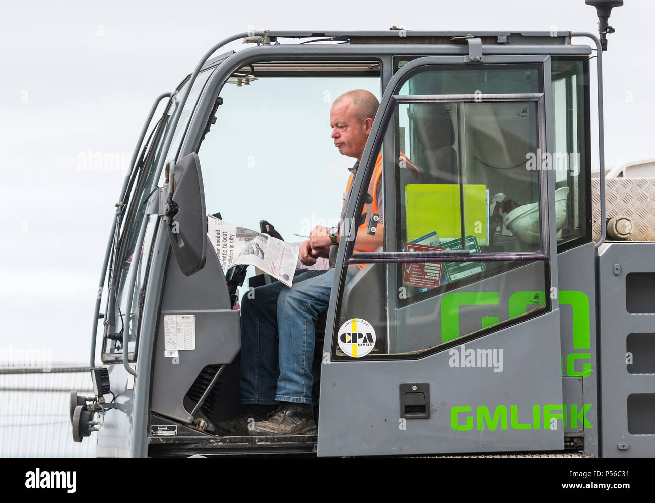 Workman sitting in construction vehicle reading a newspaper while taking a break from work, in the UK. Stock Photo