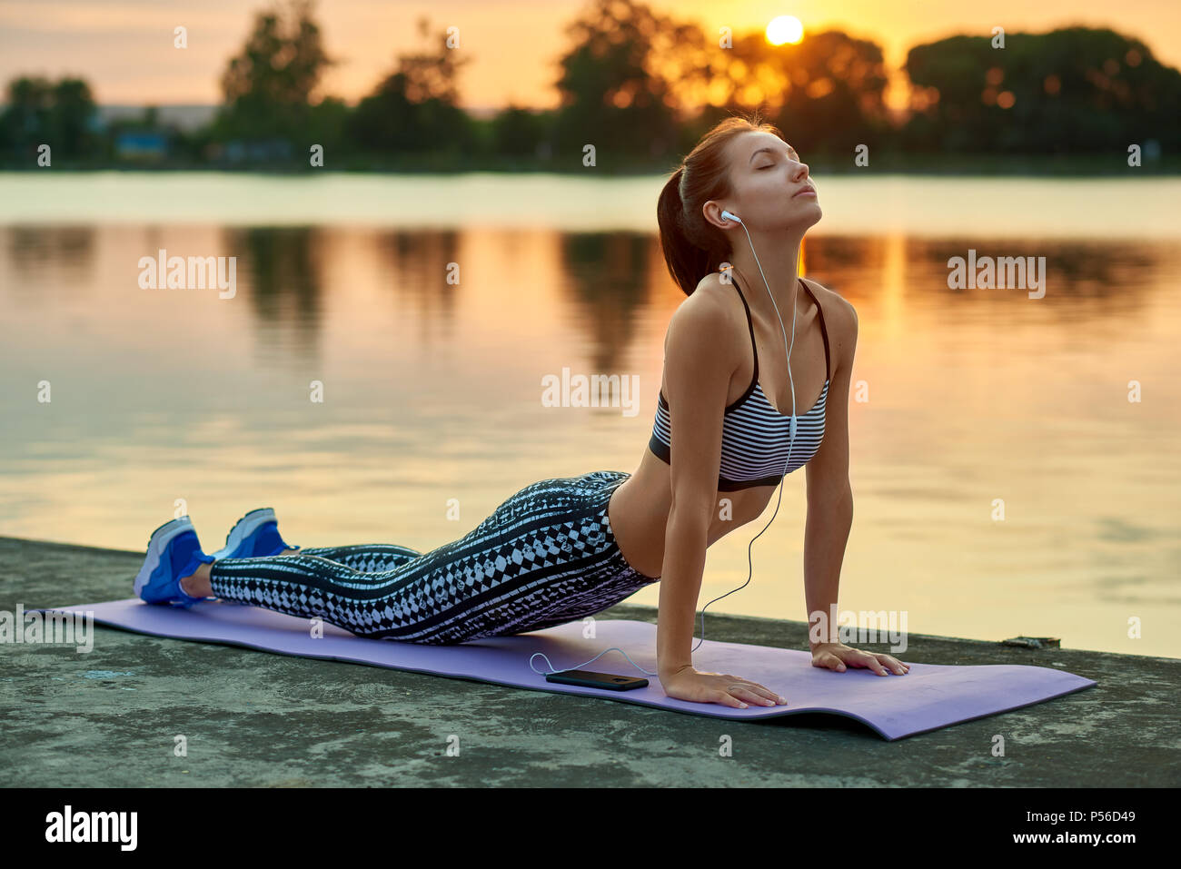 Pretty girl doing yoga exercises white summer sunset near city ...