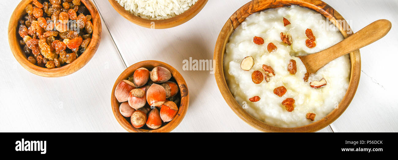 Rice milk porridge with nuts and raisins in wooden bowls on a white wooden table Stock Photo