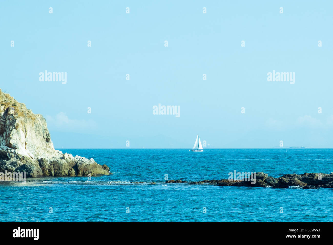 Two small rock islands in open sea connected with narrow isthmus. Lonely sailing boat with white sails . Beautiful romantic landscape, seascape. Stock Photo