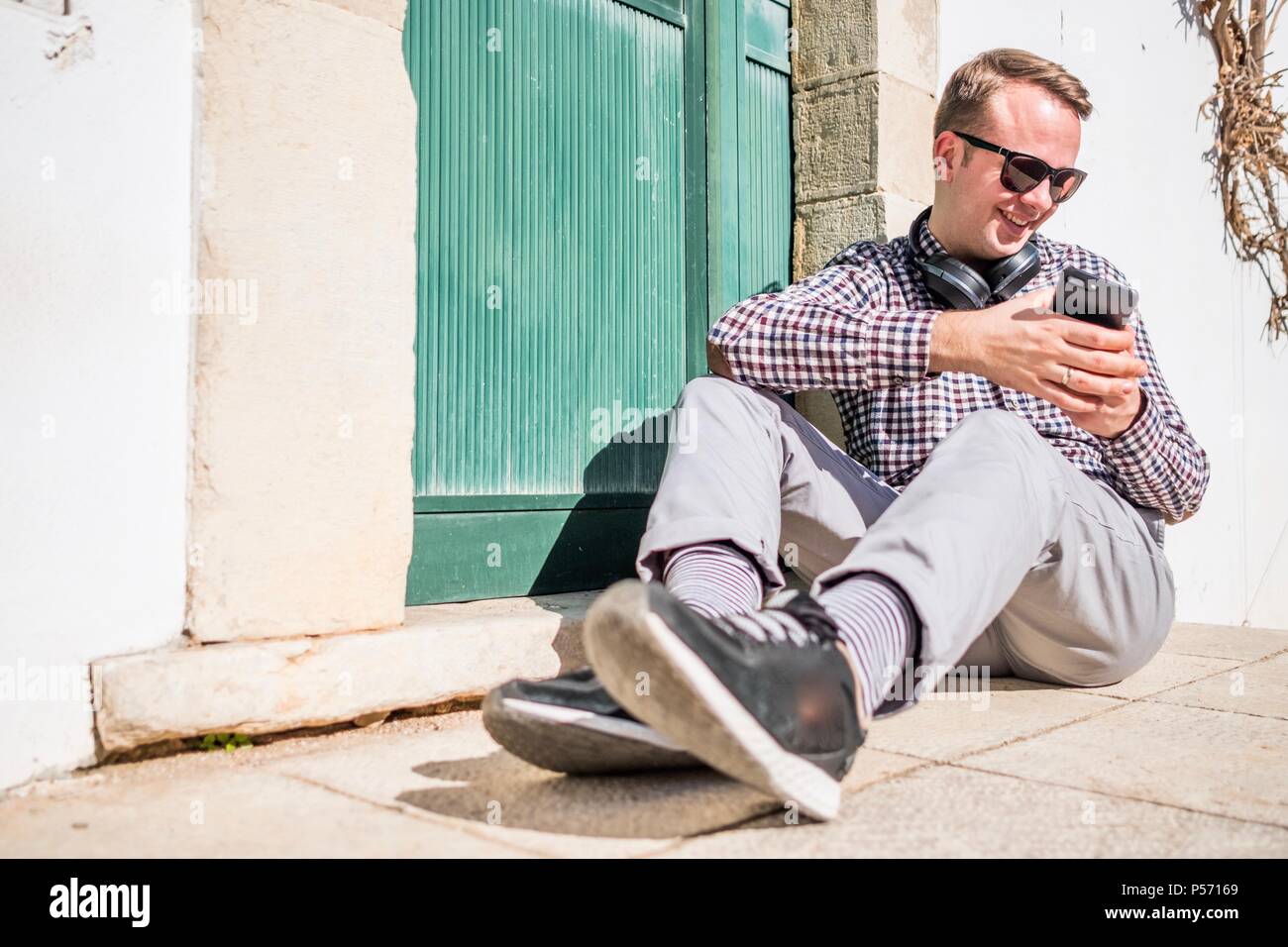 Lifestyle photo of young guy with sunglasses, headphone and smartphone in urban setting Stock Photo