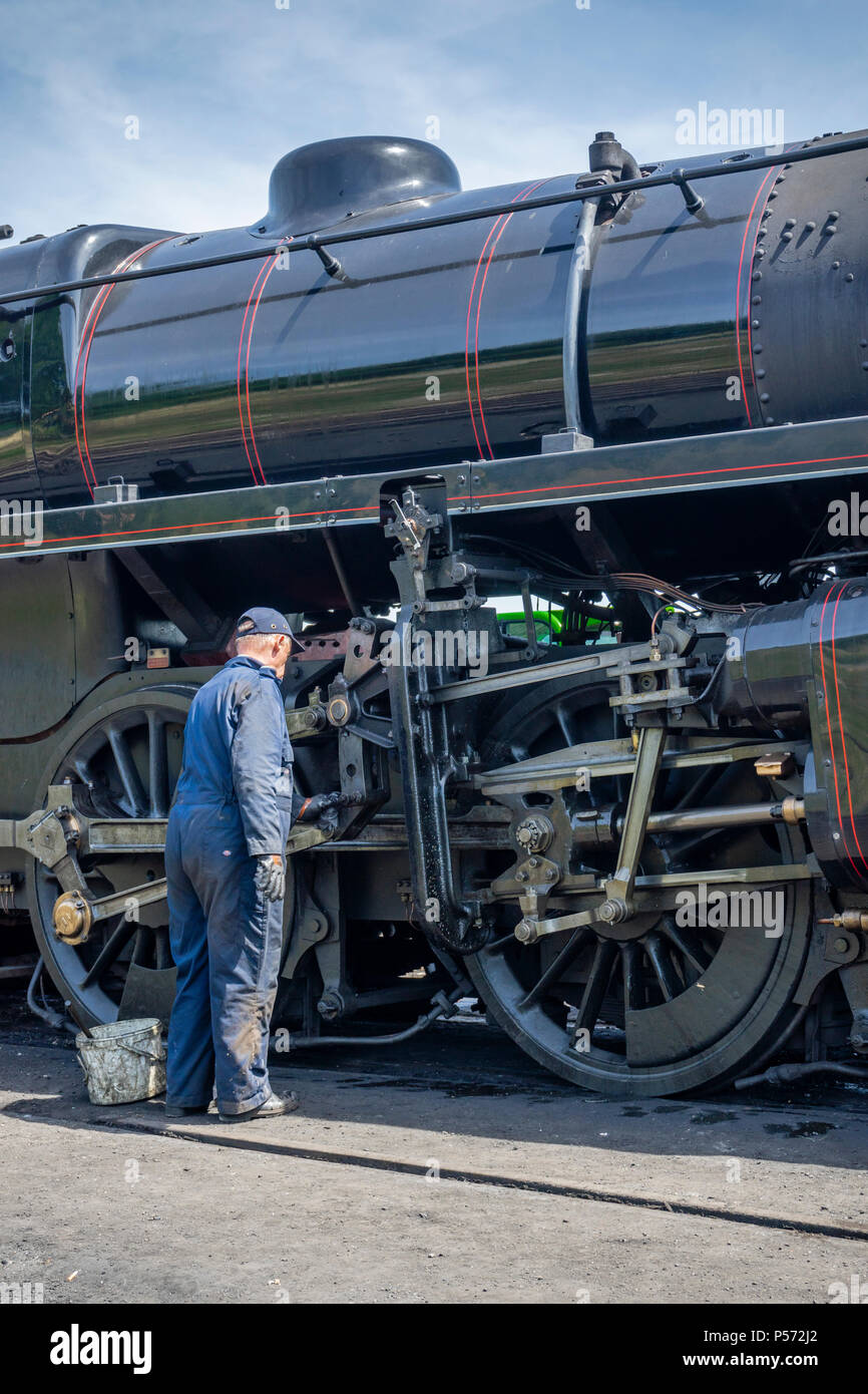 Man cleaning in traditional historic outfit / servicing a Steam locomotive of the Watercress Line in Ropley, Hampshire, UK Stock Photo
