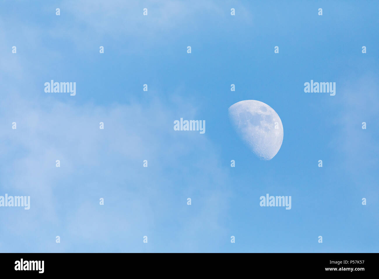 Half Moon showing during the day against blue sky with clouds surrounding it Stock Photo