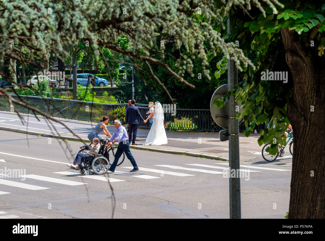 Strasbourg, mature man pushing elderly woman in wheelchair, woman cyclist, pedestrian crossing, new-weds, photographer, street, Alsace, Europe Stock Photo