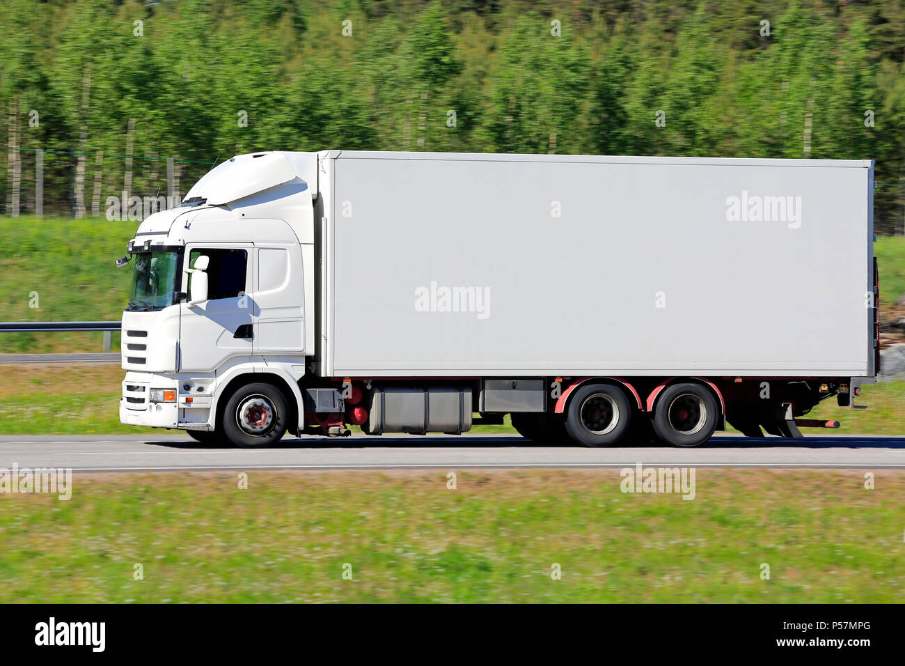 White refrigerated delivery truck on road at speed in the summer against green background. Stock Photo