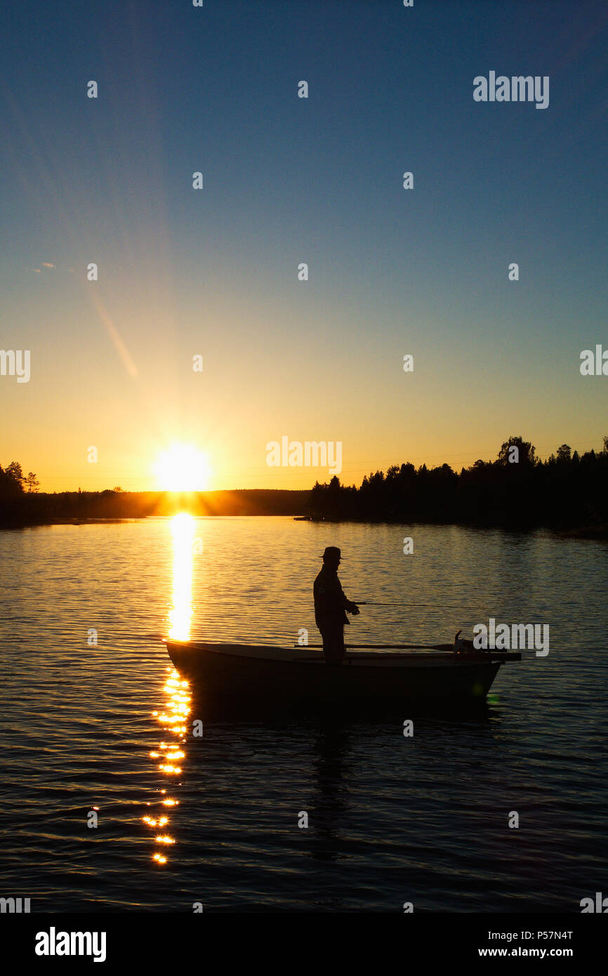 Silhouette image of a man standing and fishing in a rowing boat in