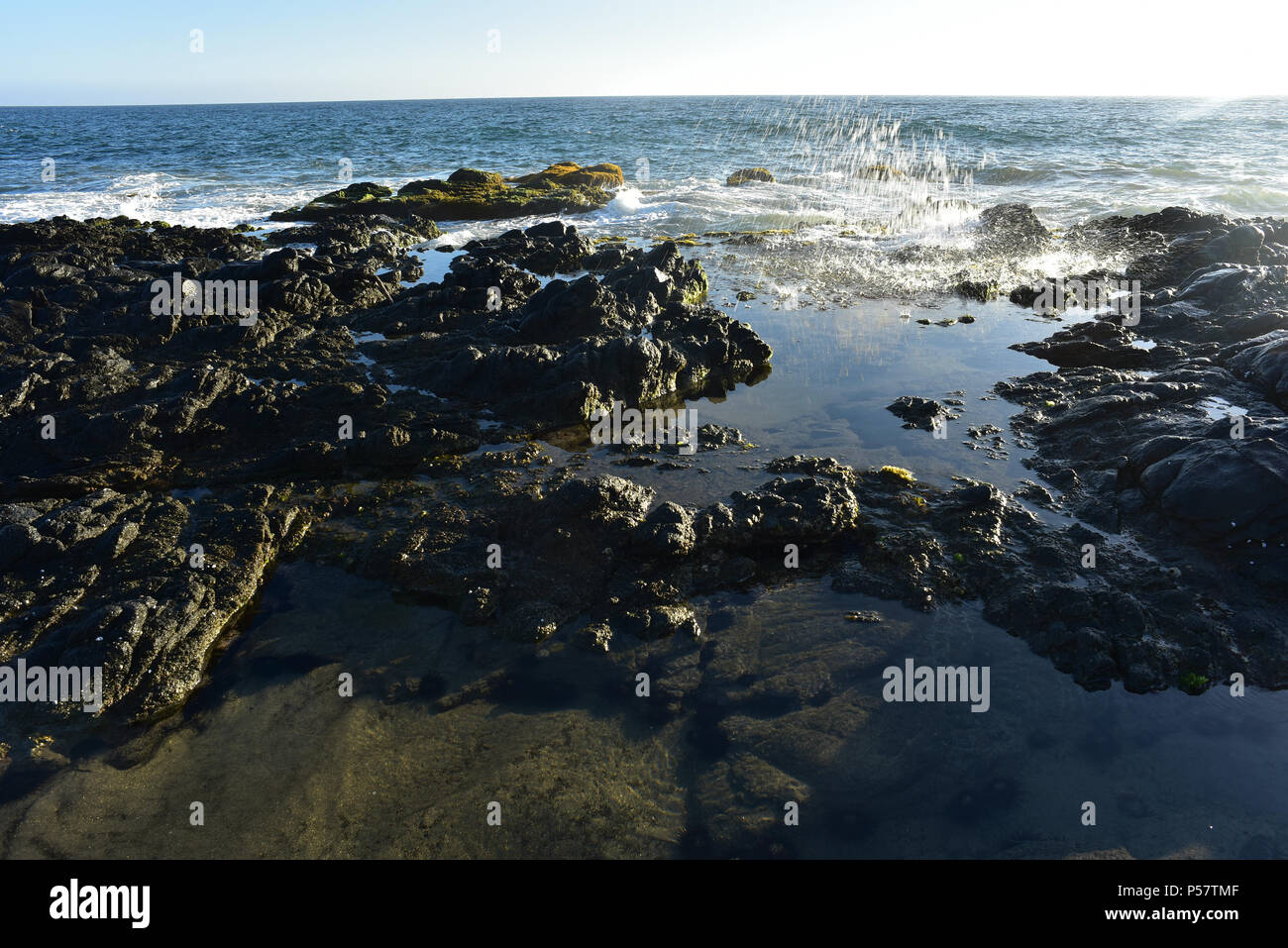 splashing wave of pacific reflected in calm tidal pool amid rocks Stock Photo