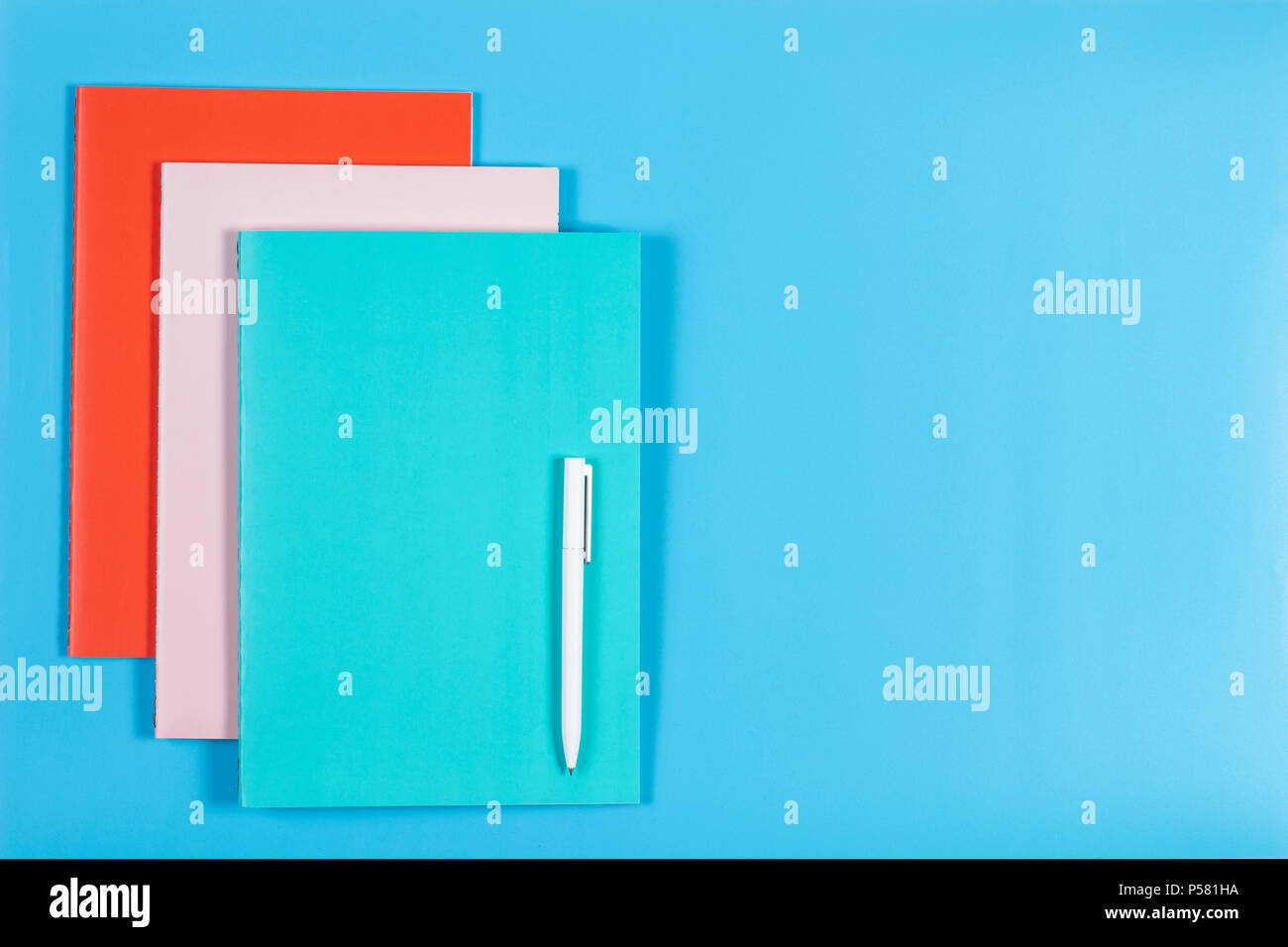 Colorful notebooks and white pen on blue background Stock Photo