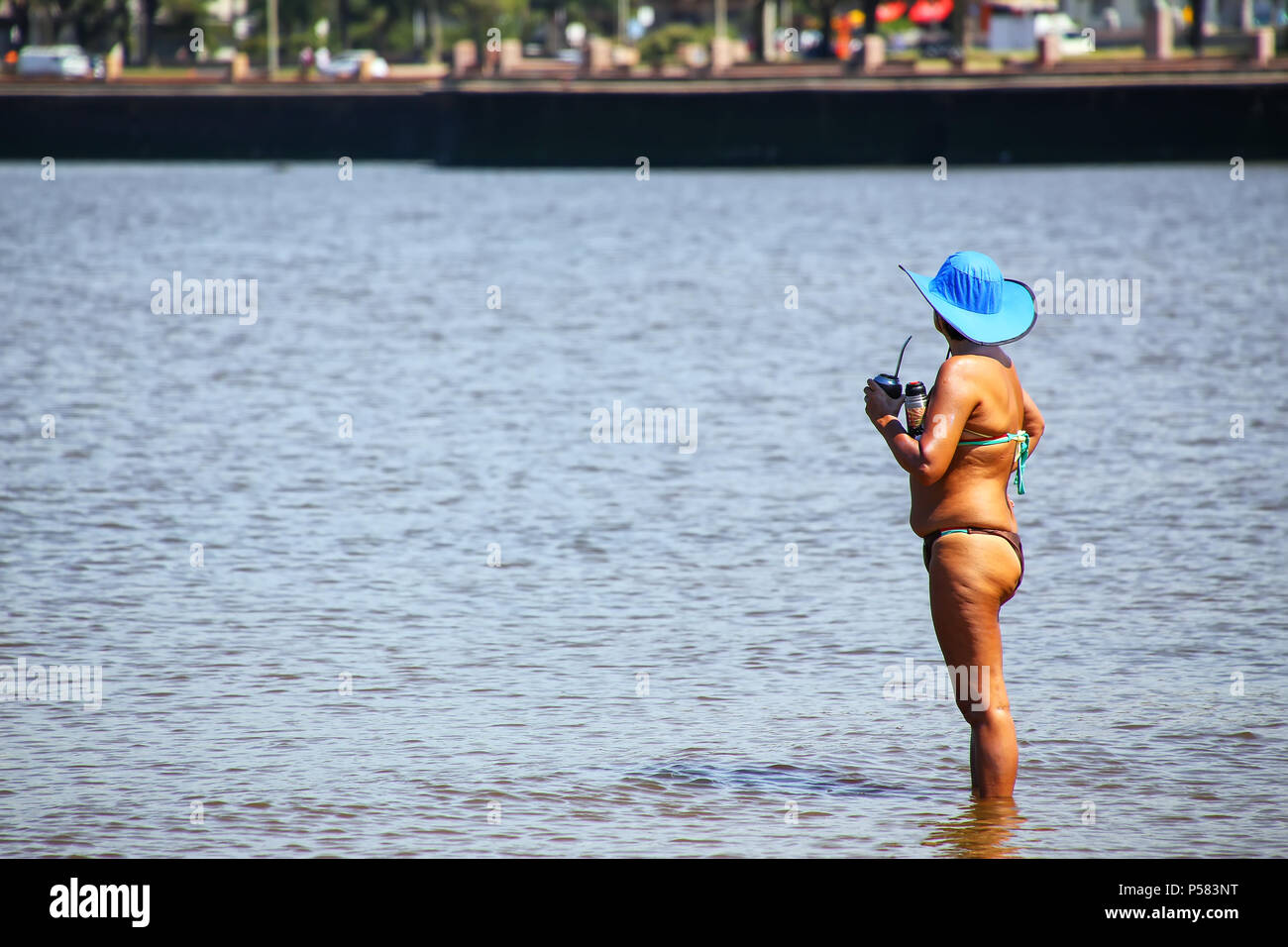 Local woman standing with mate cup by the shore of Rio de la Plata in Montevideo, Uruguay. Montevideo is the capital and the largest city of Uruguay Stock Photo