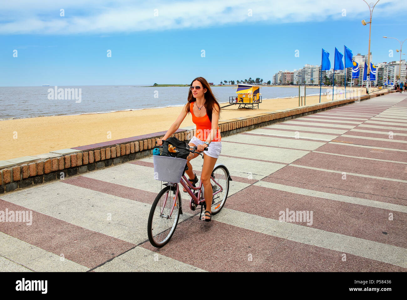 Woman biking on the boulevard along Pocitos beach in Montevideo, Uruguay. Montevideo is the capital and the largest city of Uruguay Stock Photo