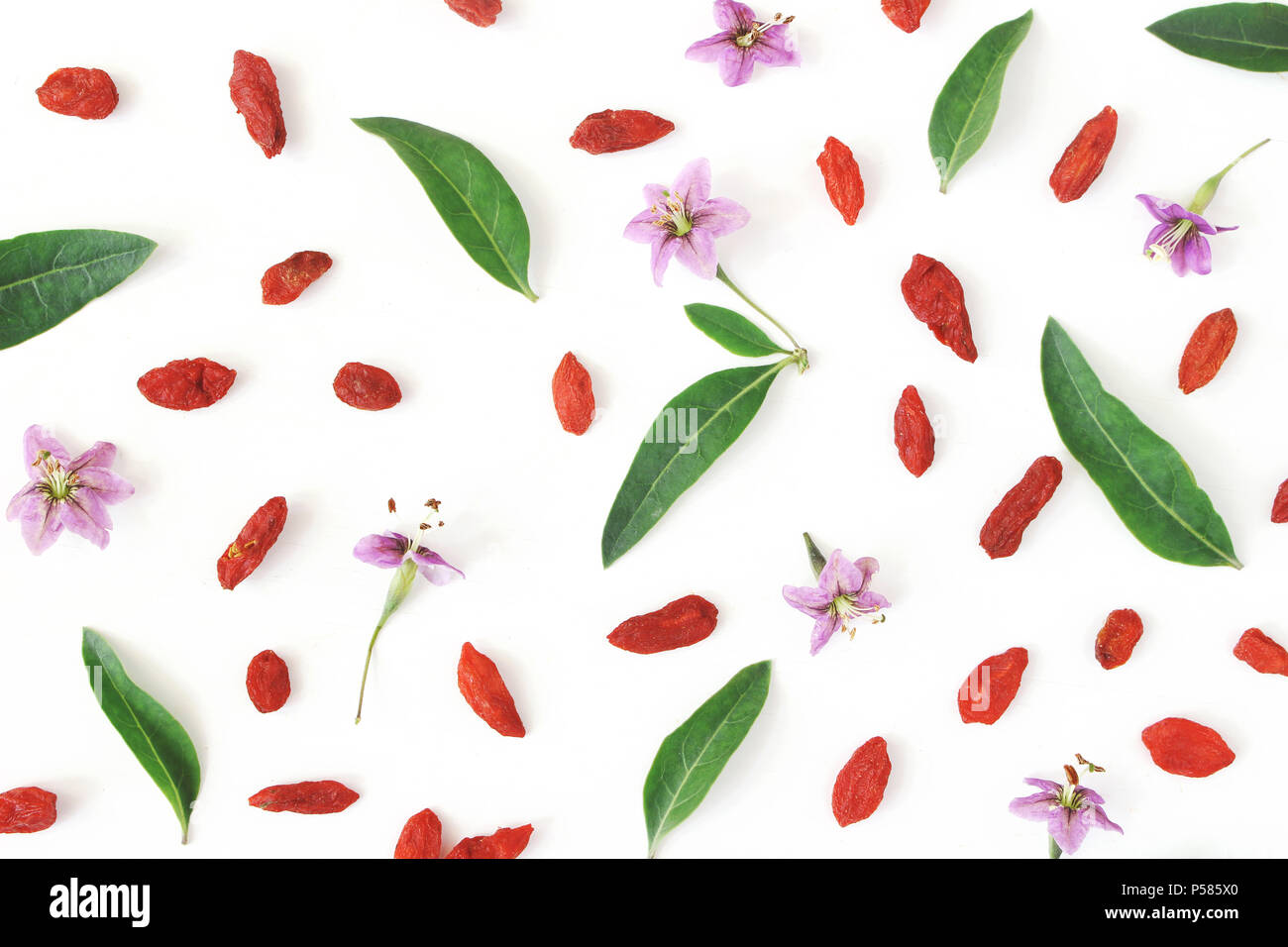 Closeup of Goji berries, Lycium barbarum. Dried Asian fruit, leaves and blossoms isolated on white wooden background. Healthy superfood. Floral pattern. Flatlay, top view. Stock Photo