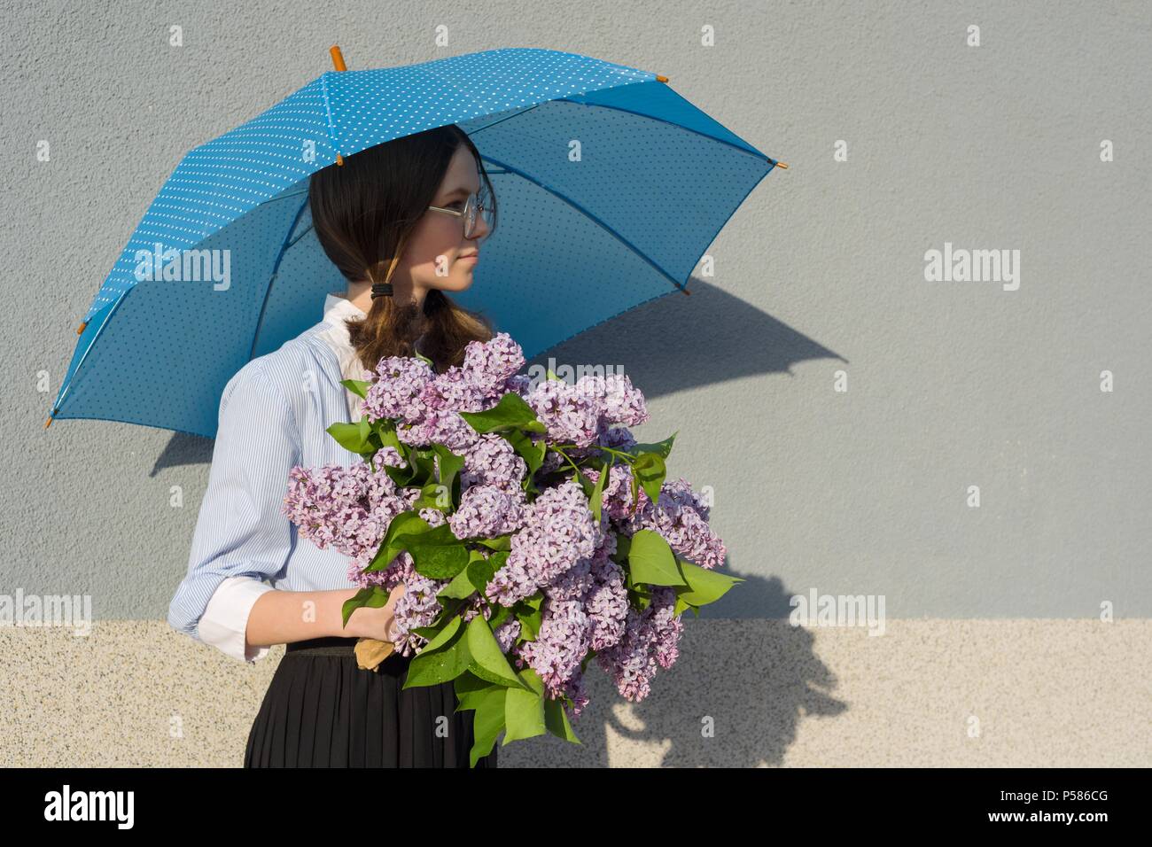 Profile portrait romantic teenage girl with bouquet of lilacs, with an umbrella on gray wall background. Outdoor, copy space Stock Photo