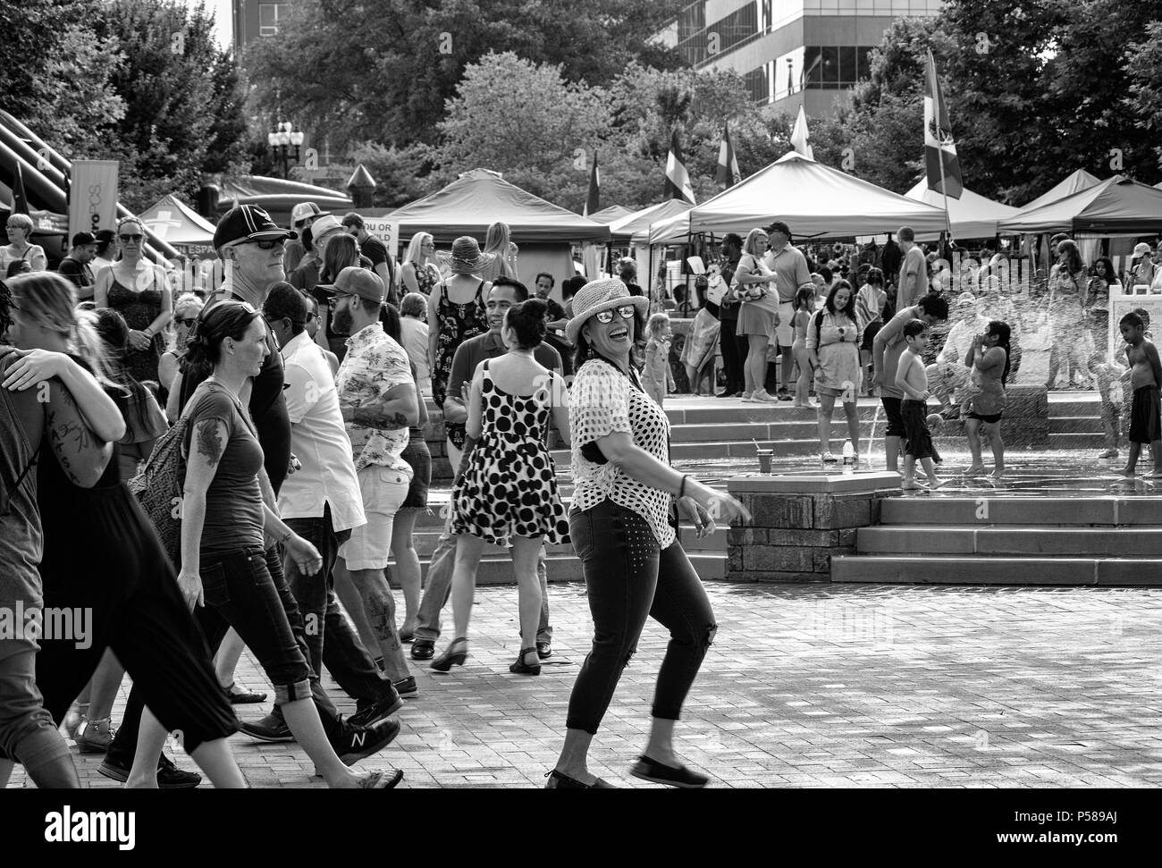 A woman laughs at the photographer, walking in the crowd in front of children playing in the water feature in Asheville, NC, USA, at Hola Carolina Stock Photo