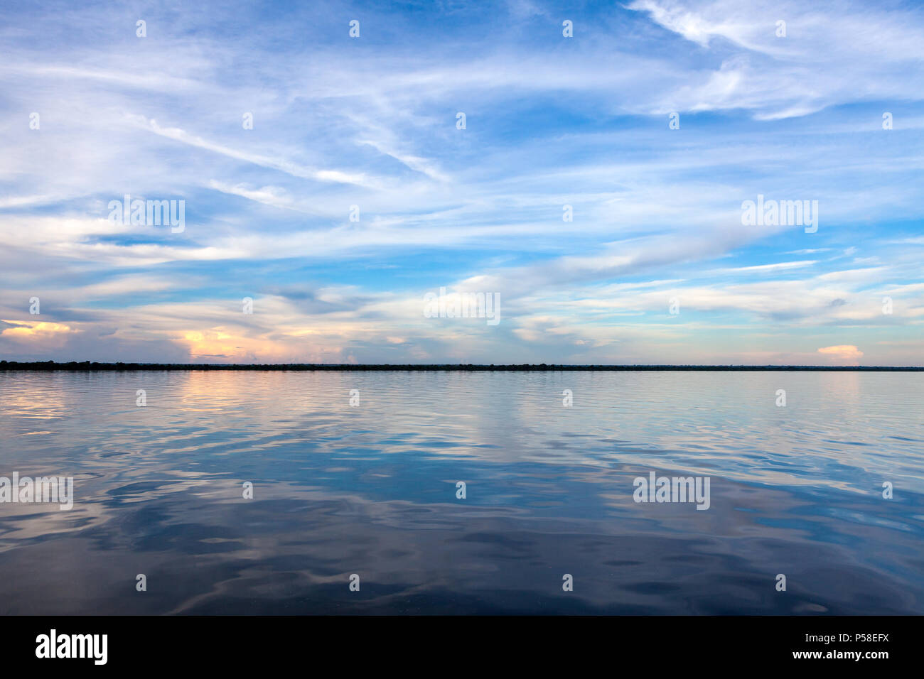 Amazonas, Brazil - River bank in the Amazon rainforest with textured dark waters of Negro river reflecting blue sky and clouds and the forest in the b Stock Photo