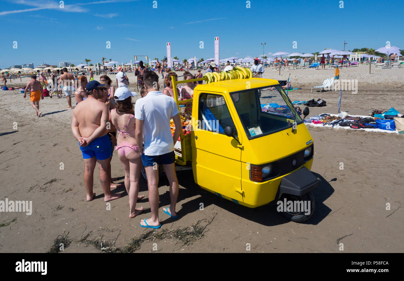 Sottomarina, Italy - June 23, 2018: Fruit seller with yellow vehicle on three wheels on the beach. Stock Photo