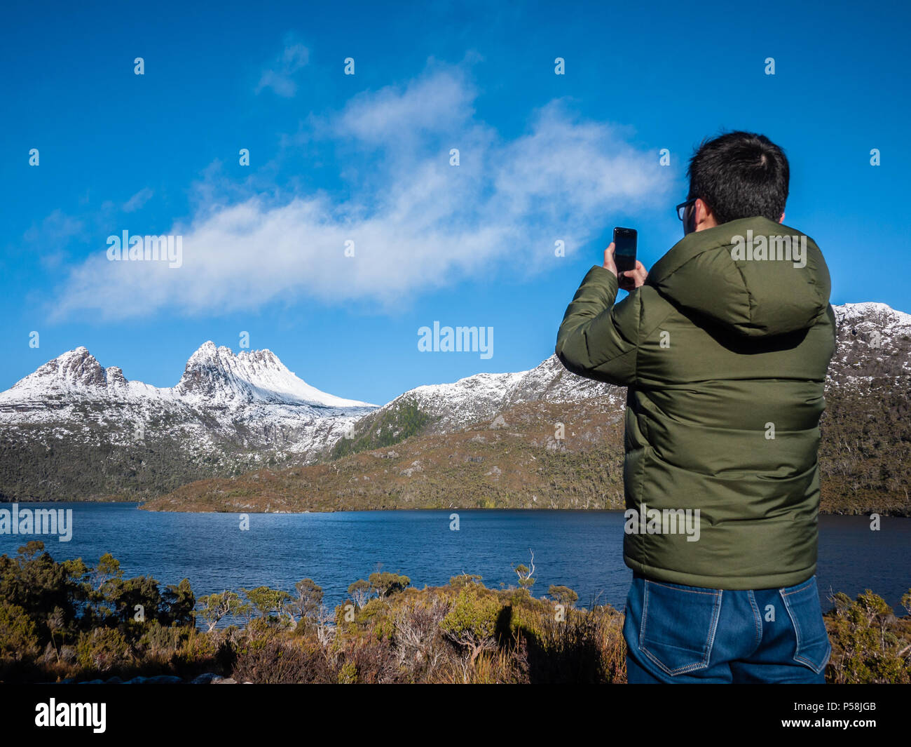 A Chinese male tourist taking photo with mobile phone of the Cradle Mountain by Dove Lake -- a famous and popular attraction in Tasmania, Australia. Stock Photo