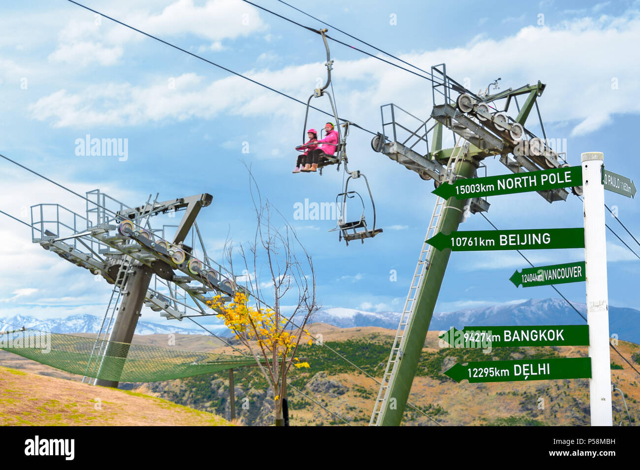 Queenstown, NZ – April 15, 2018: Fun riders with their carts on a cable chair lift going up the hill top for a luge ride with mountains and snow. Stock Photo