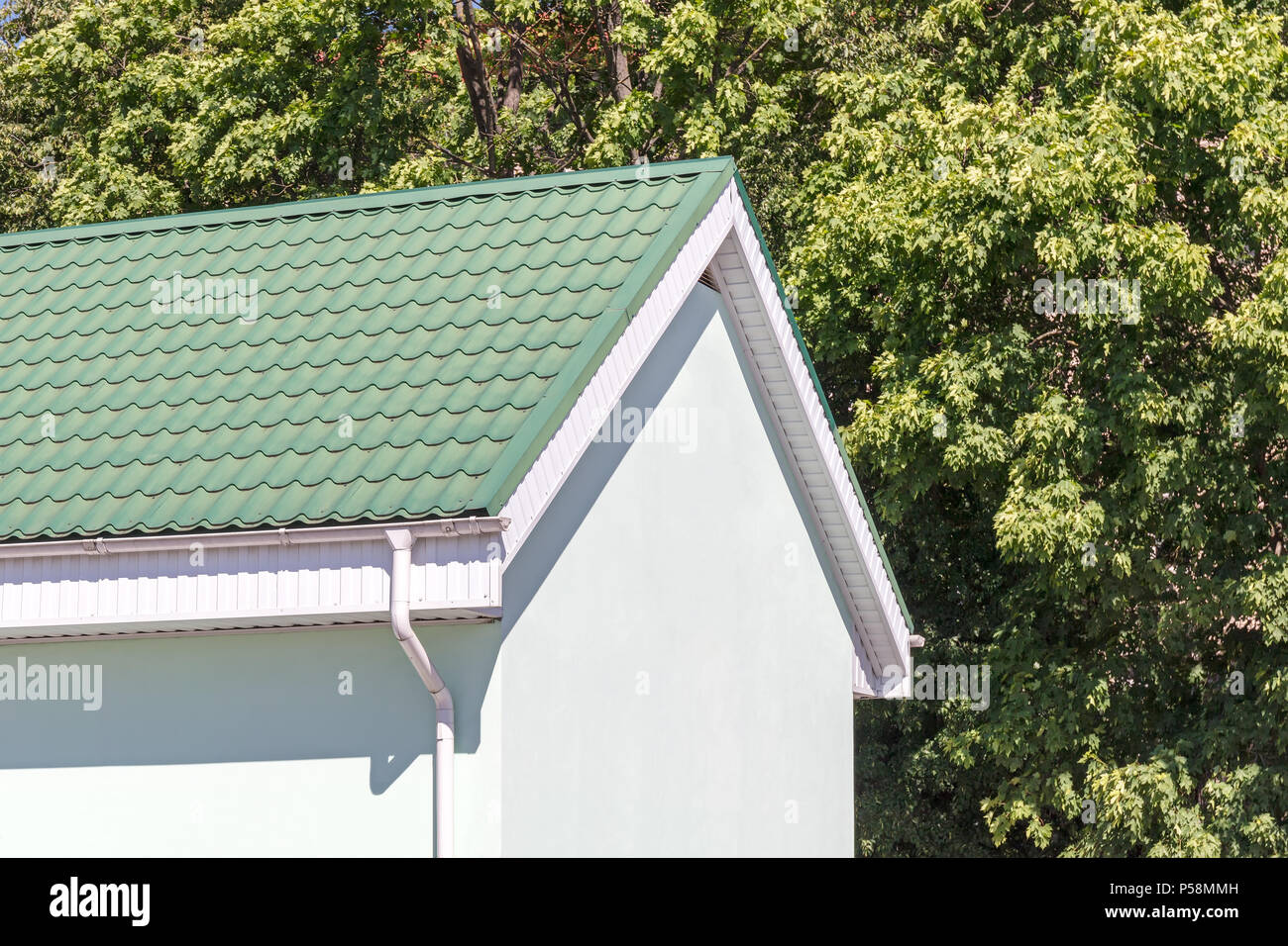 house with green tiled metal roof and white rain gutter on summer trees