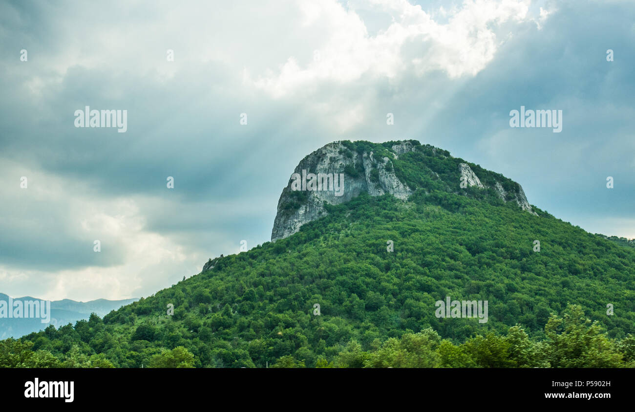 Clouds in an overcast sky after the rain, letting through beams of sunlight, shining down on a lush mountaintop. Majestic landscape in Croatia. Stock Photo