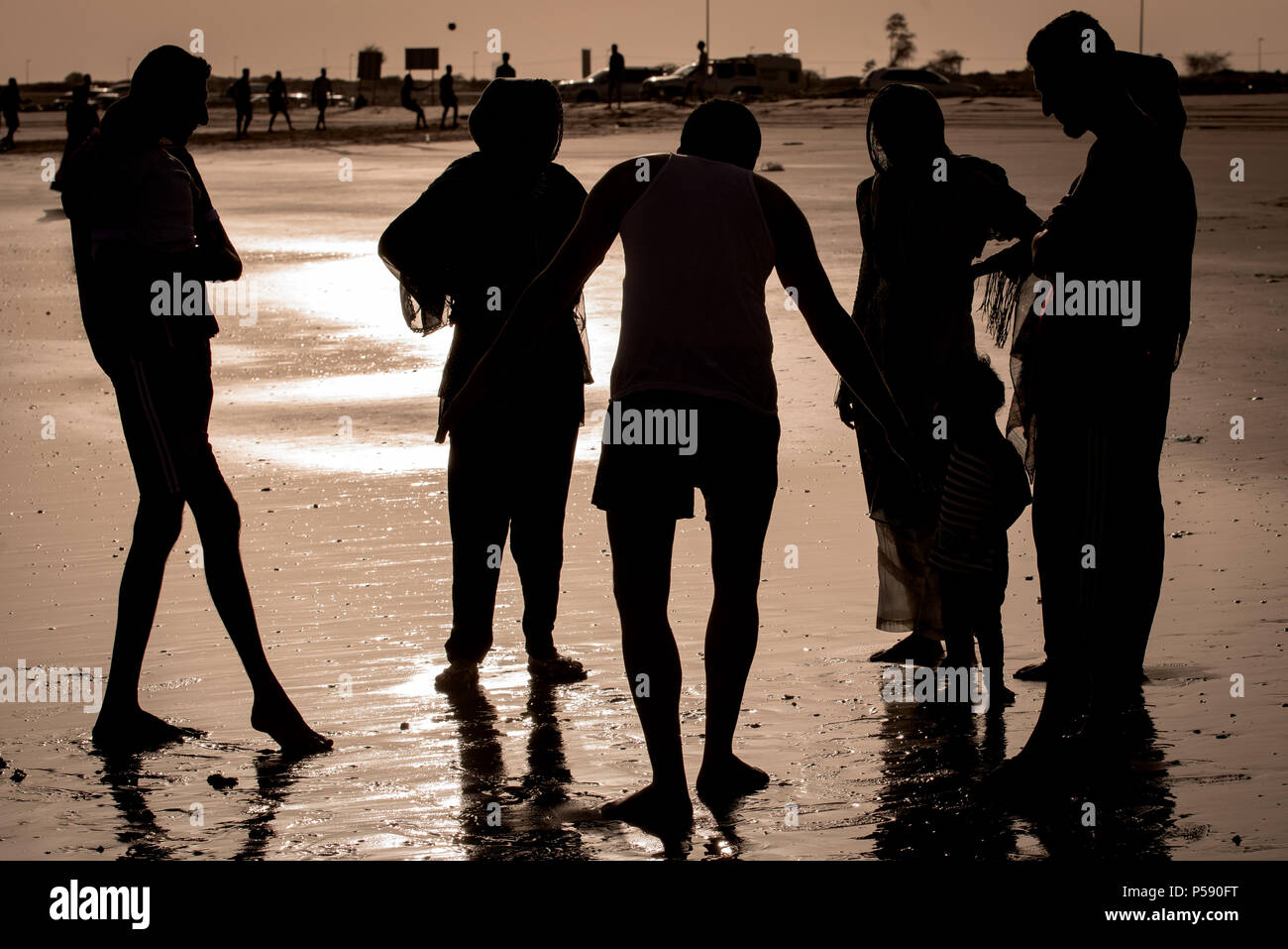 Silhouette of young adults against shining sand at Umm Al Quwain beach Stock Photo