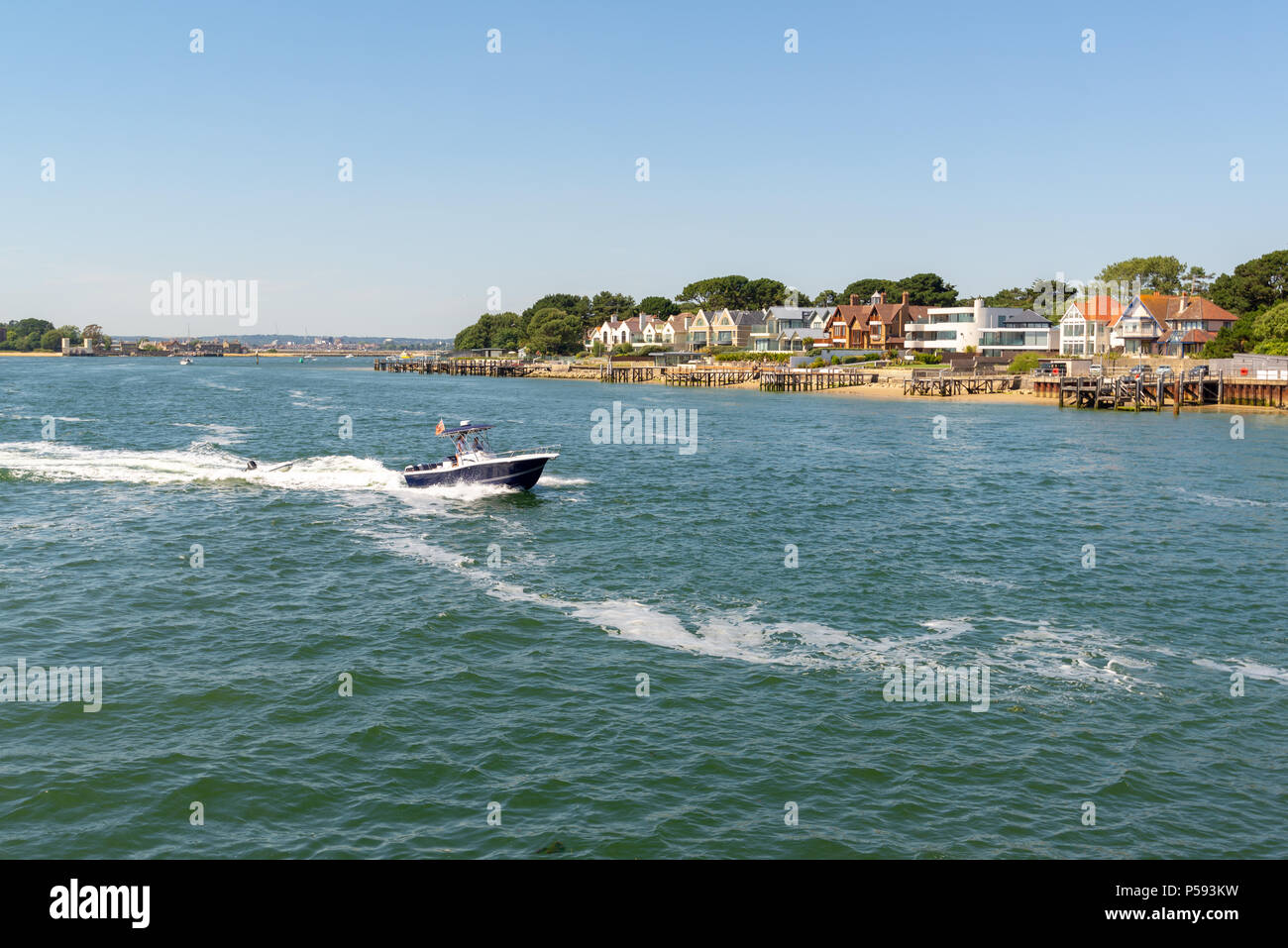 Boat speeding out of Poole Harbour, Dorset, England, UK and past some exclusive seafront property on the Sandbanks peninsula. Stock Photo
