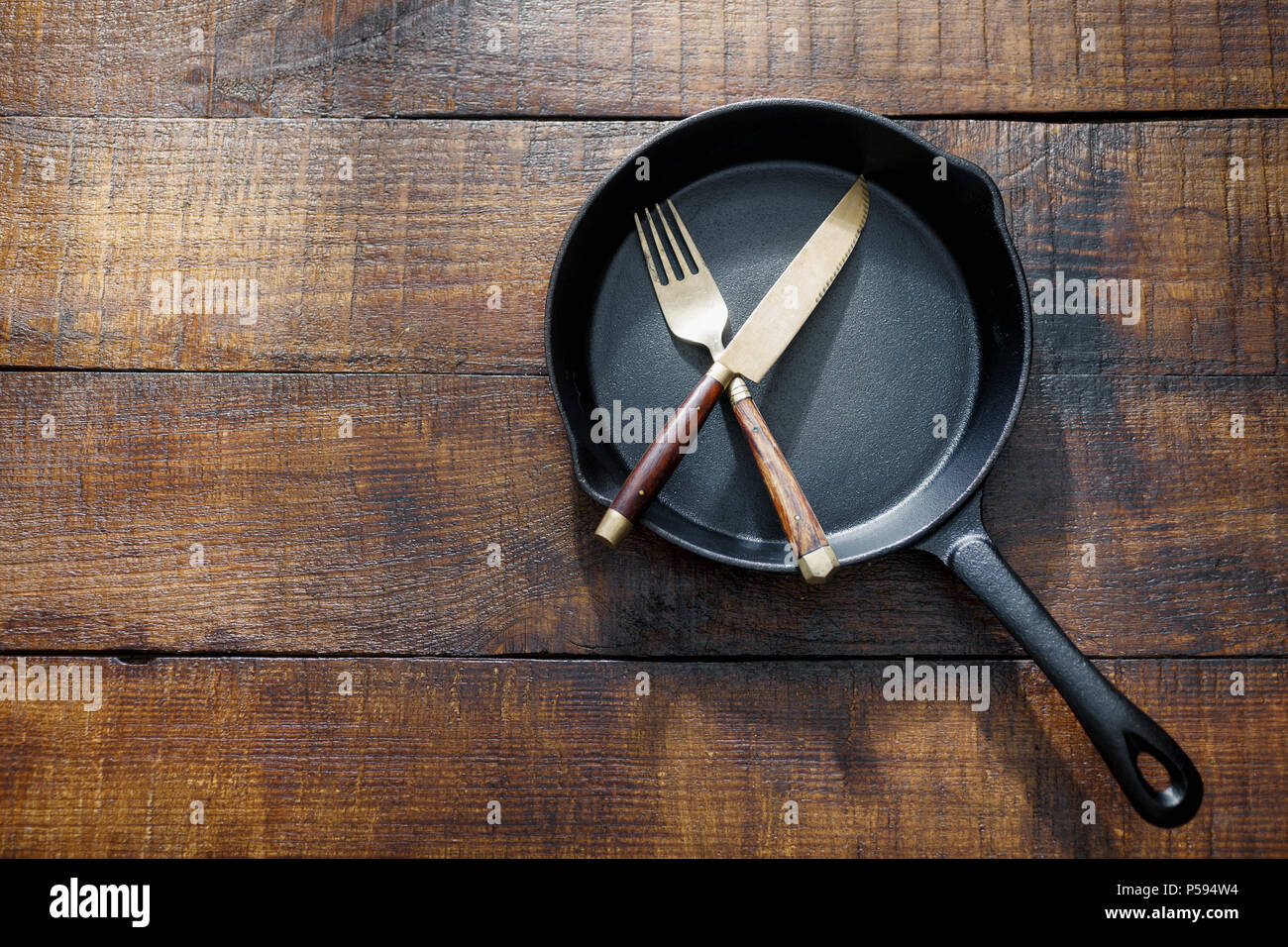 Small cast-iron frying pan with fork and knife on vintage wooden table, top view Stock Photo