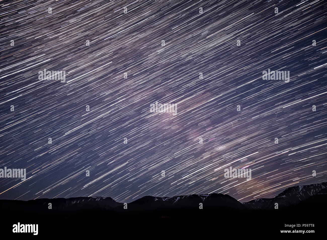 A beautiful night panorama of the starry sky with traces of meteors and stars in the form of circular tracks against the background of the snowy mount Stock Photo