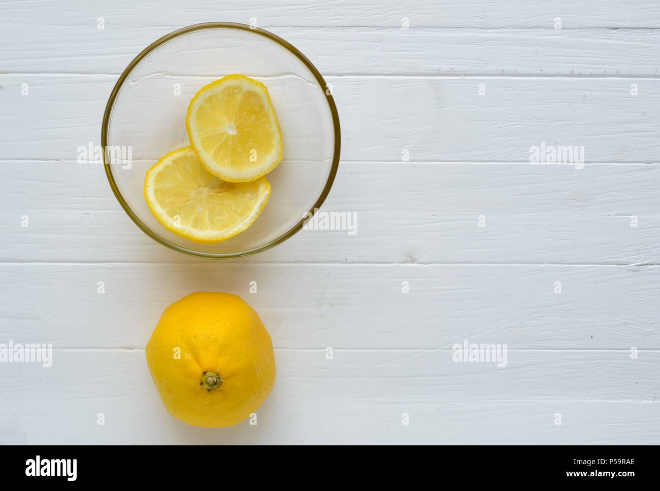 One lemon and two slices of lemon into glass plate.One lemon is down and two slices of lemon into glass plate are on top.White wooden background.Copys Stock Photo