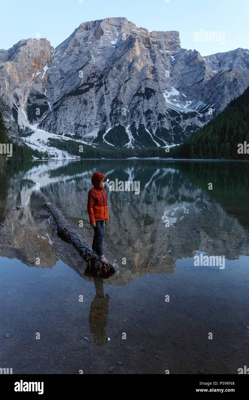 Young boy with a headlamp balancing on sunken log on lake Lago di Braies, Dolomites, Italy. Stock Photo