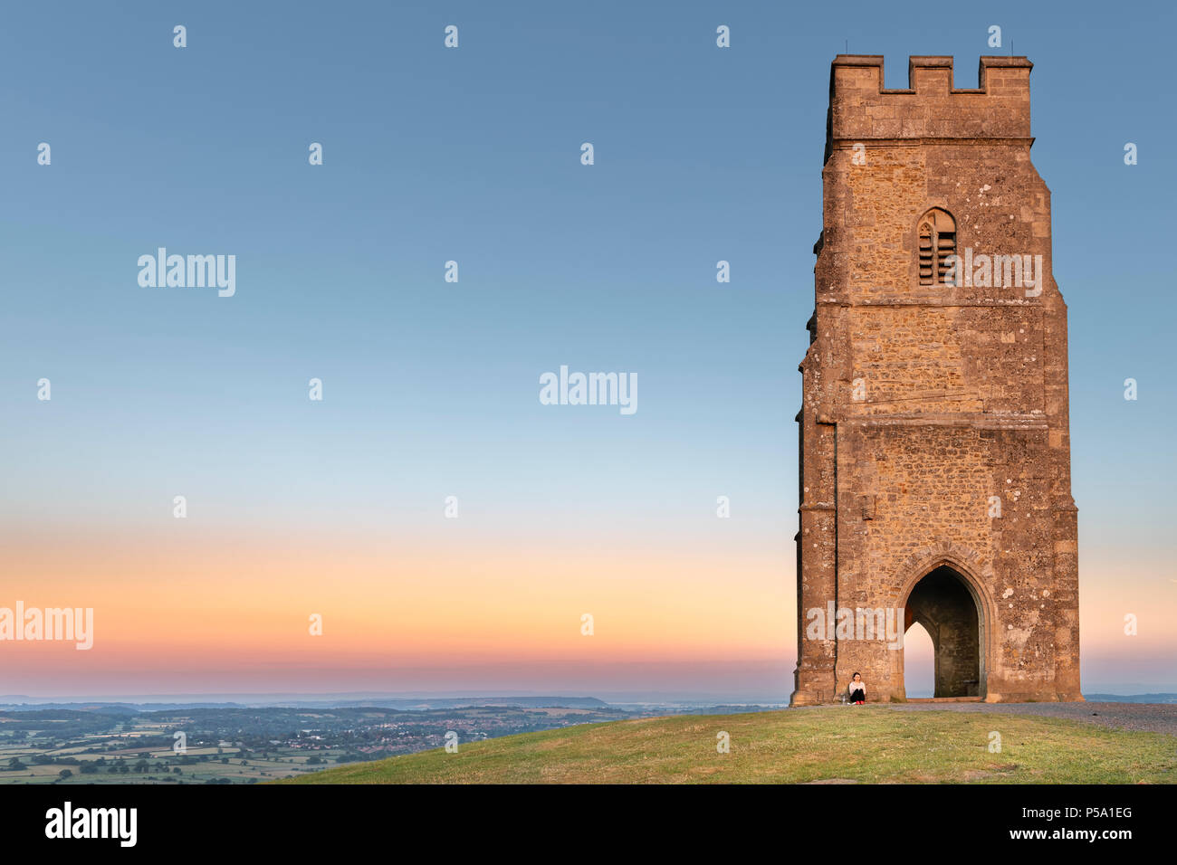 Glastonbury, Somerset, UK. 26th June, 2018. UK Weather - Sitting on top of Glastonbury Tor, a young lady watches a beautiful  sunrise over the Somerset Levels, as the West of England is set to see temperatures rise again in to the high twenties. Credit: Terry Mathews/Alamy Live News Stock Photo