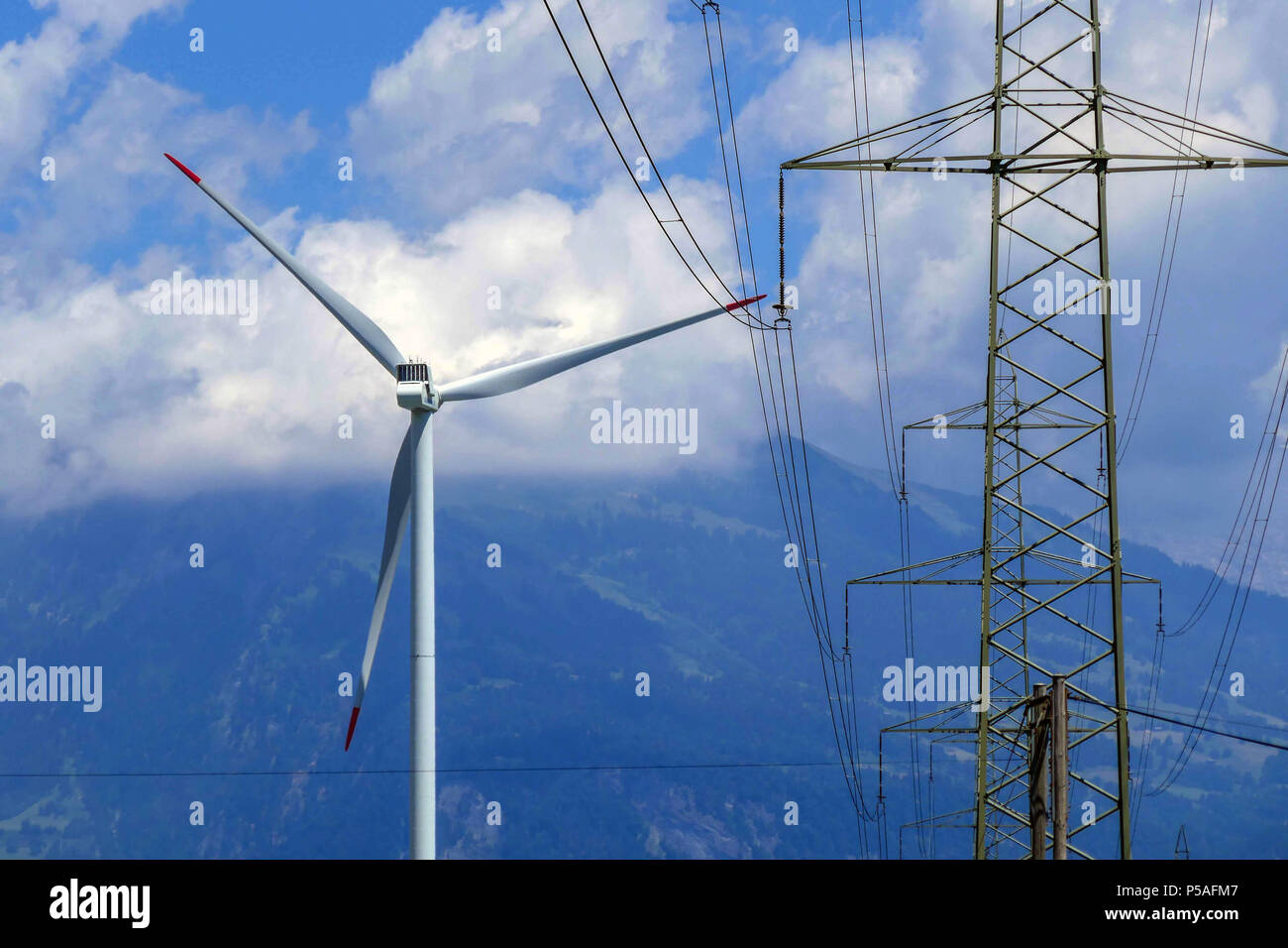 Wind turbine and electricity pylon, with clouds and mountains, Switzerland Stock Photo