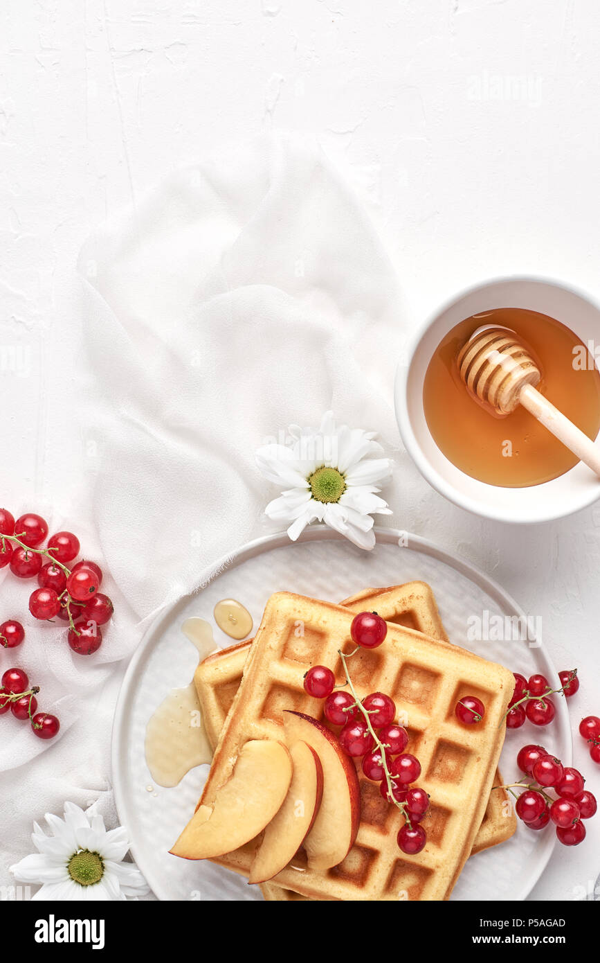 Flat lay of traditional belgian waffles with fresh fruit, nectarine, currant and honey on white background. Breakfast. Top view with copy space. Stock Photo