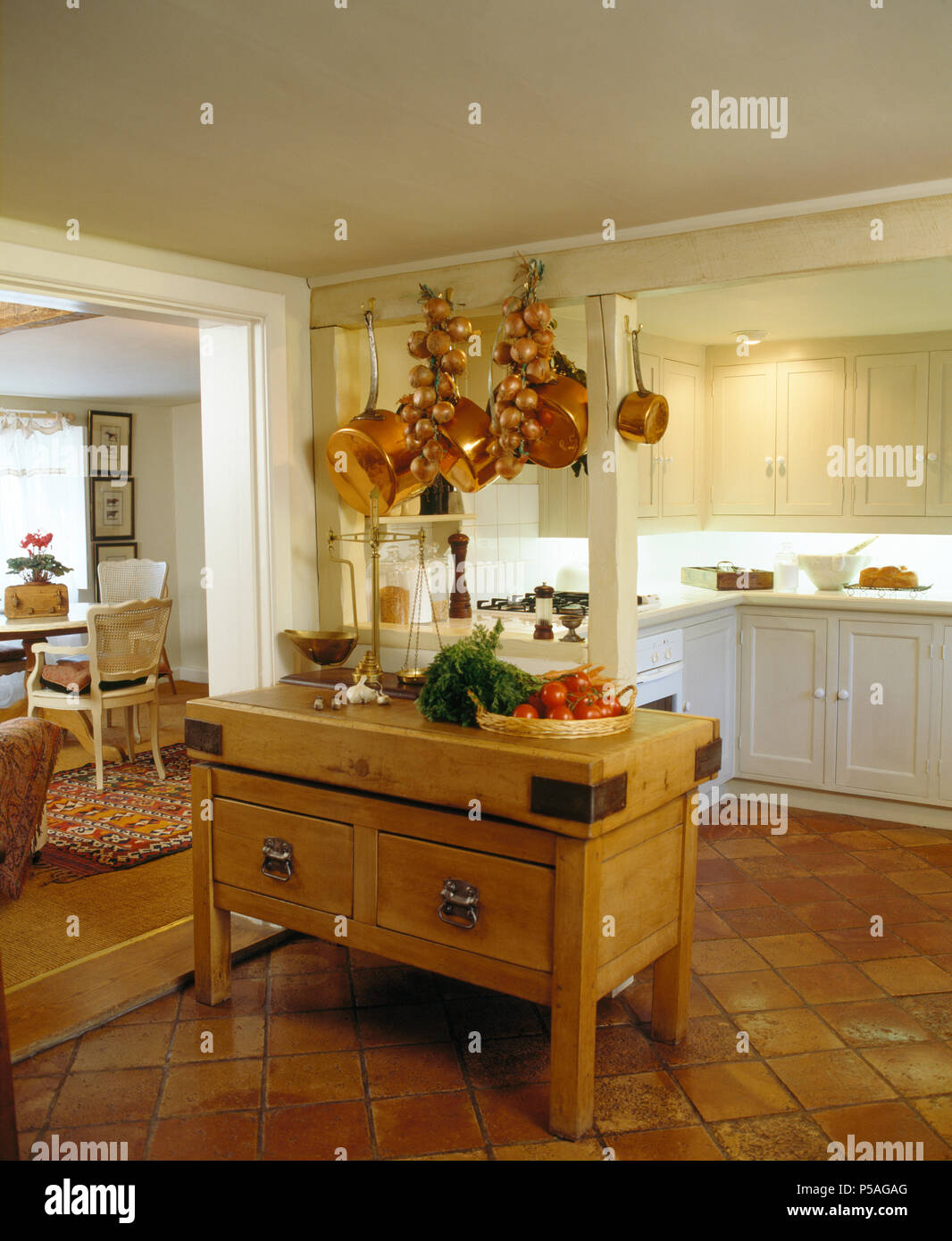 Copper pans and strings of onions hanging from beam above butcher's block in kitchen with terracotta tiled floor Stock Photo