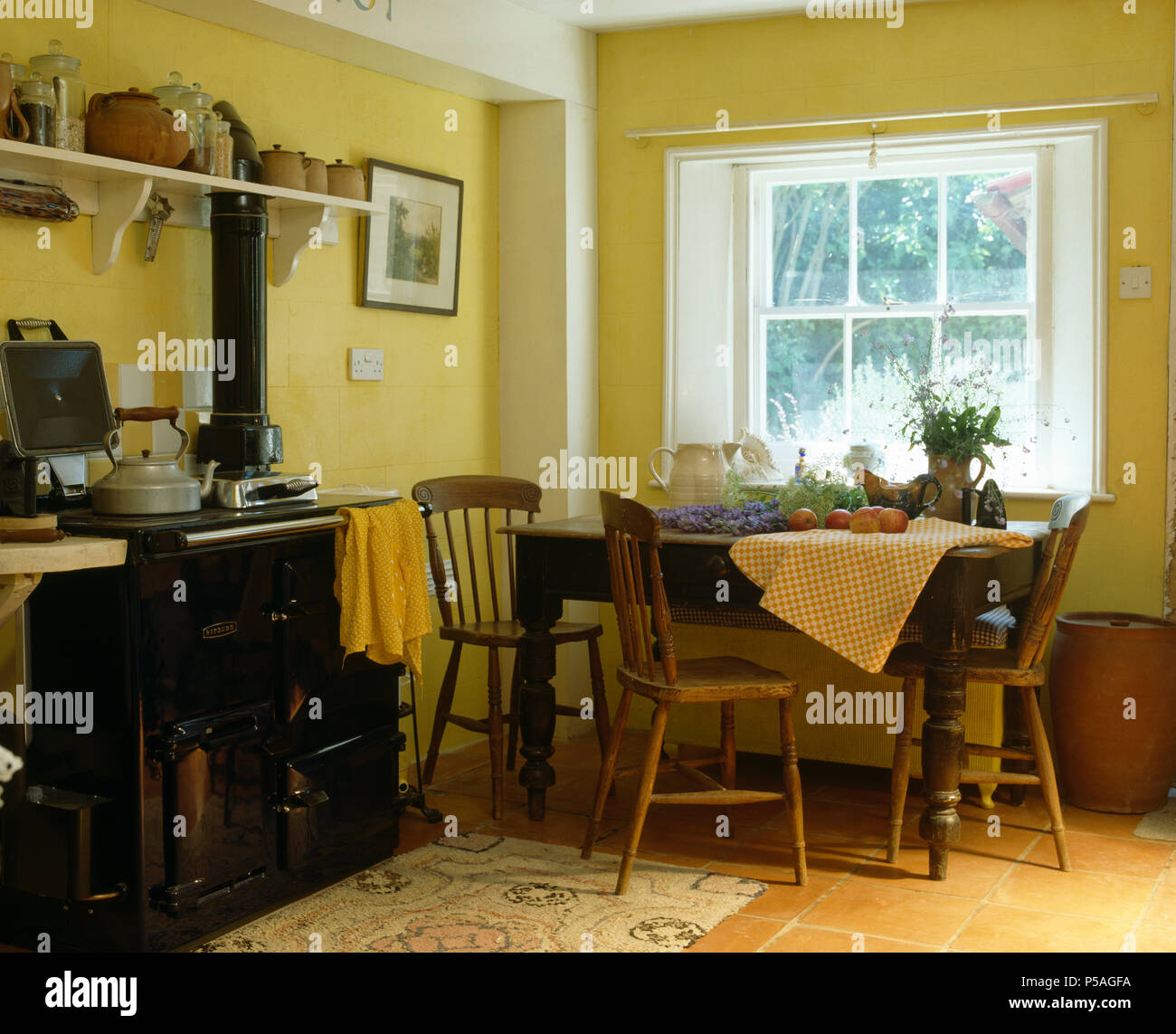 Black Rayburn oven in yellow cottage kitchen with vintage wooden table and pine chairs Stock Photo