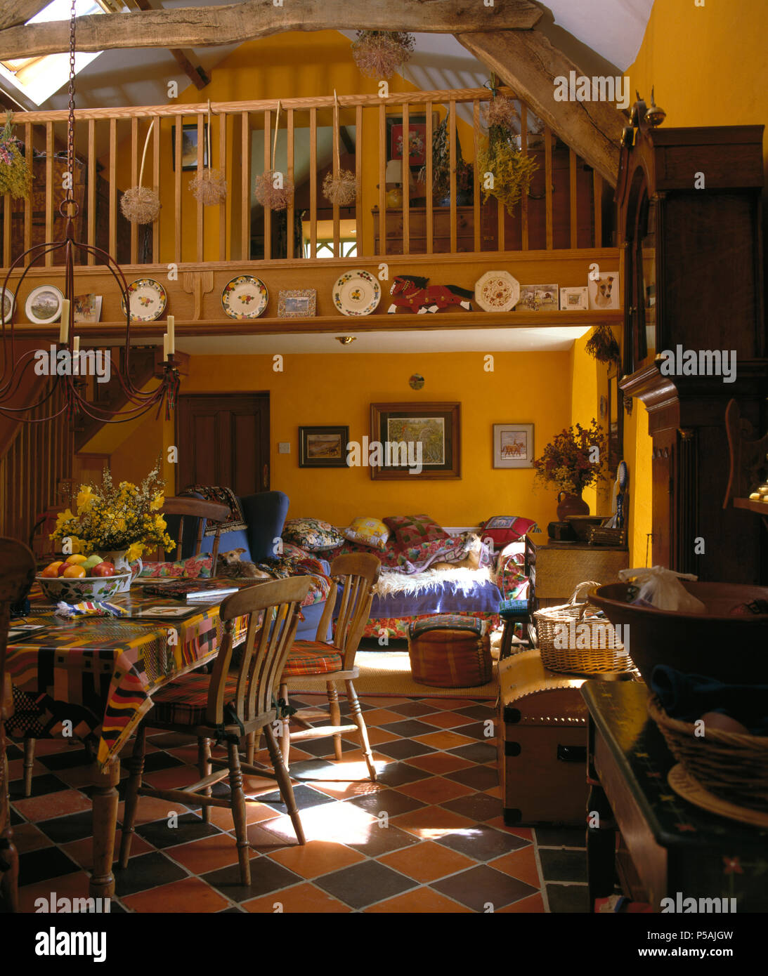 Open-plan yellow kitchen dining room in barn conversion with comfortable sofa below mezzanine floor Stock Photo