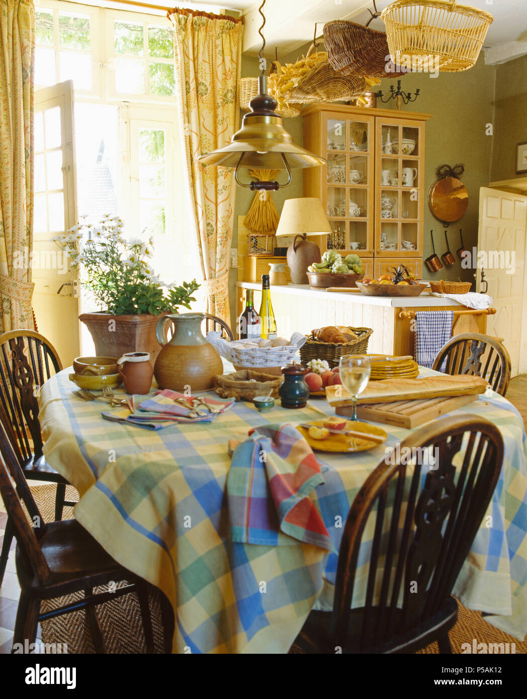 Antique Windsor chairs at table with checked cloth set for breakfast in country kitchen Stock Photo