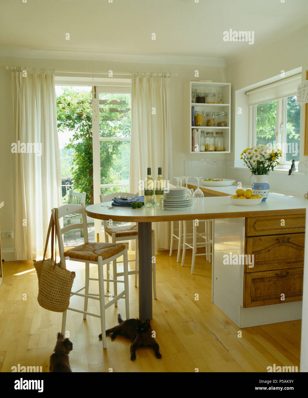 Rush-seated stool at breakfast bar in white country kitchen with French windows and wooden flooring Stock Photo