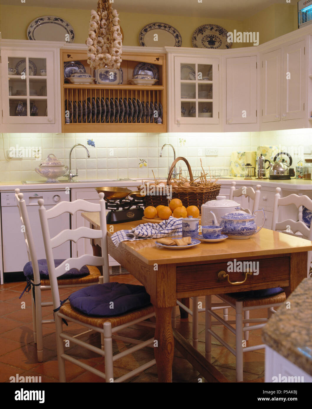 White painted ladder-back chairs at pine table in white country kitchen Stock Photo