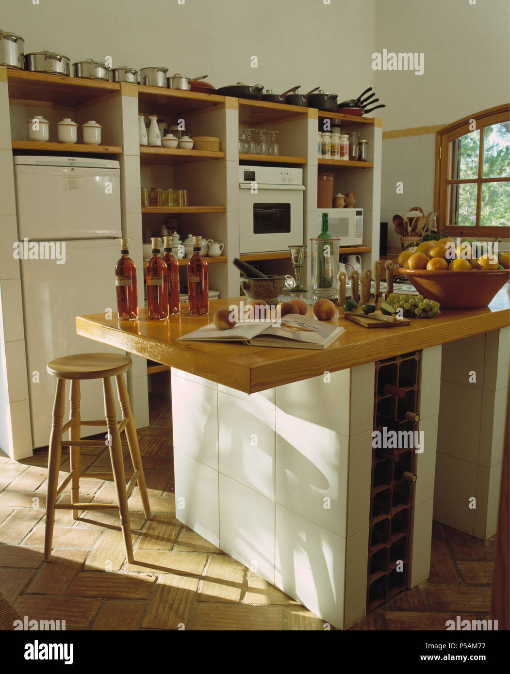 Bottles of oil on wooden worktop of island unit in Greek coastal kitchen with brick flooring Stock Photo